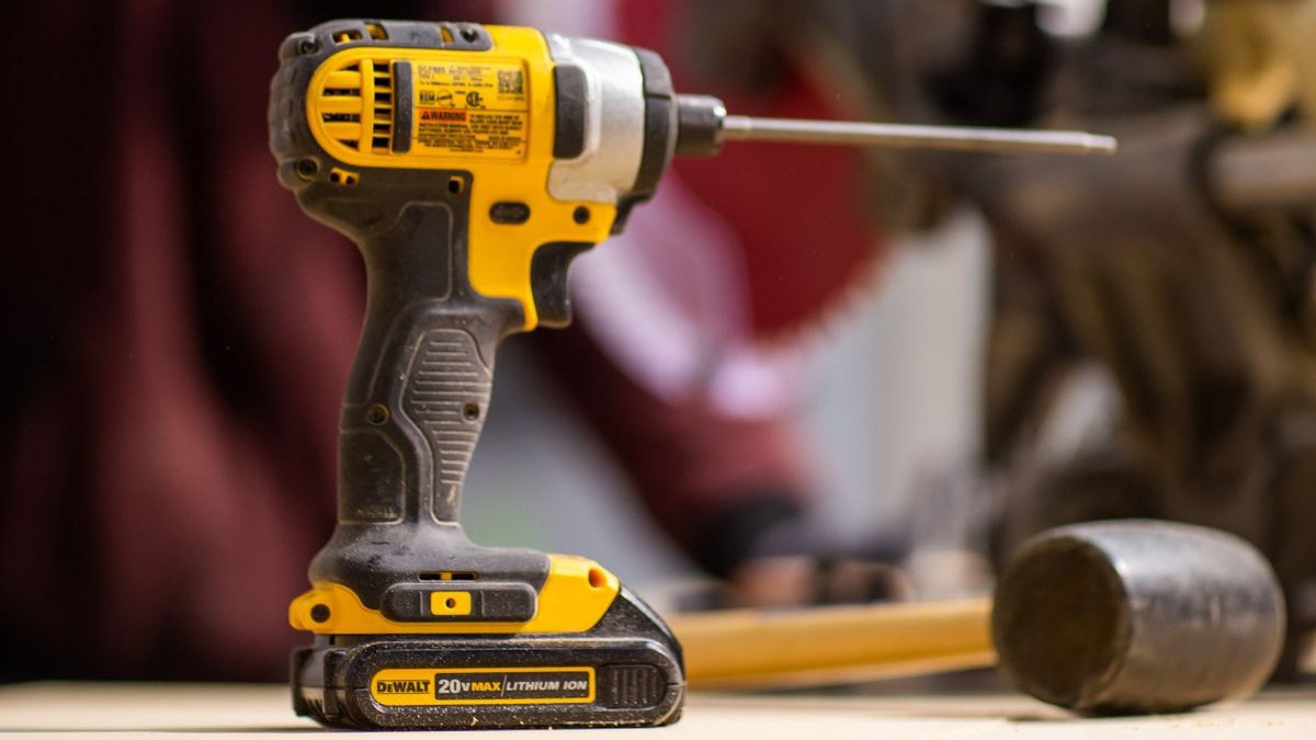 A well-used cordless drill standing on a workbench with a rubber mallet behind it