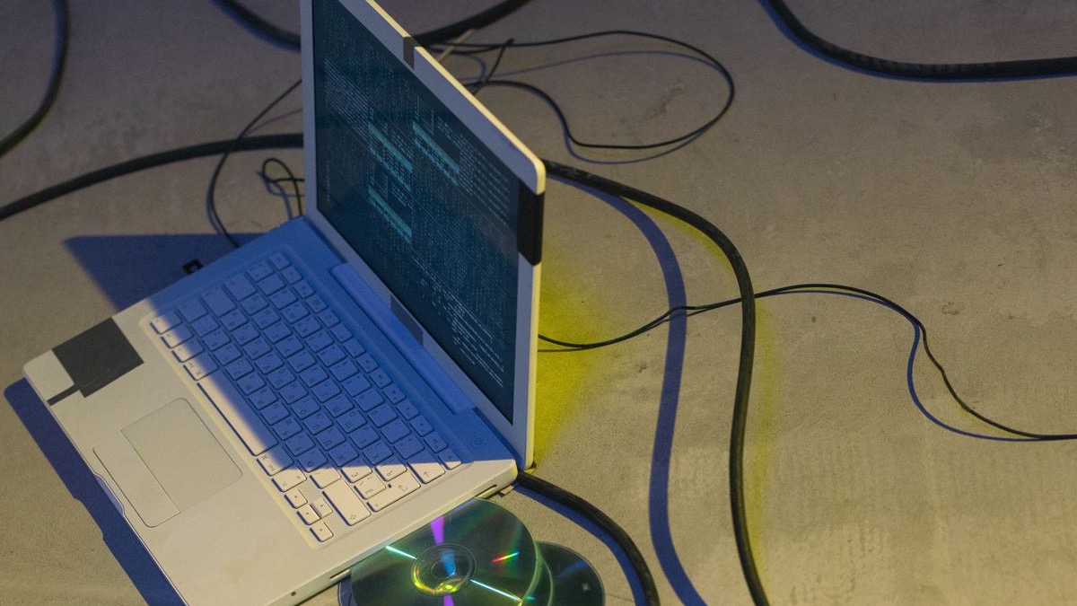 An old white laptop showing a terminal screen, surrounded by cables and CDs
